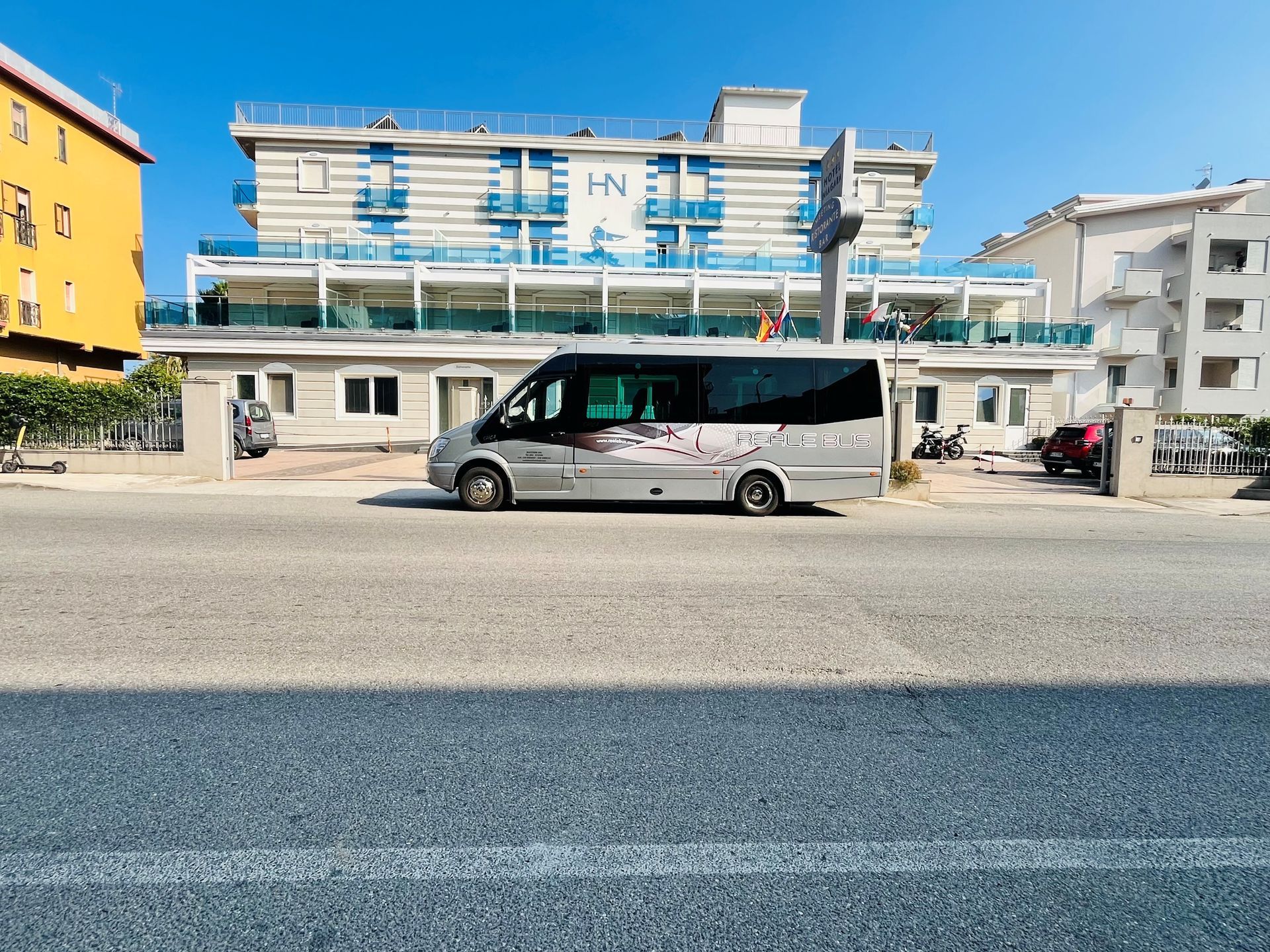 Minibus bianco parcheggiato in una strada soleggiata davanti a un edificio blu e bianco.