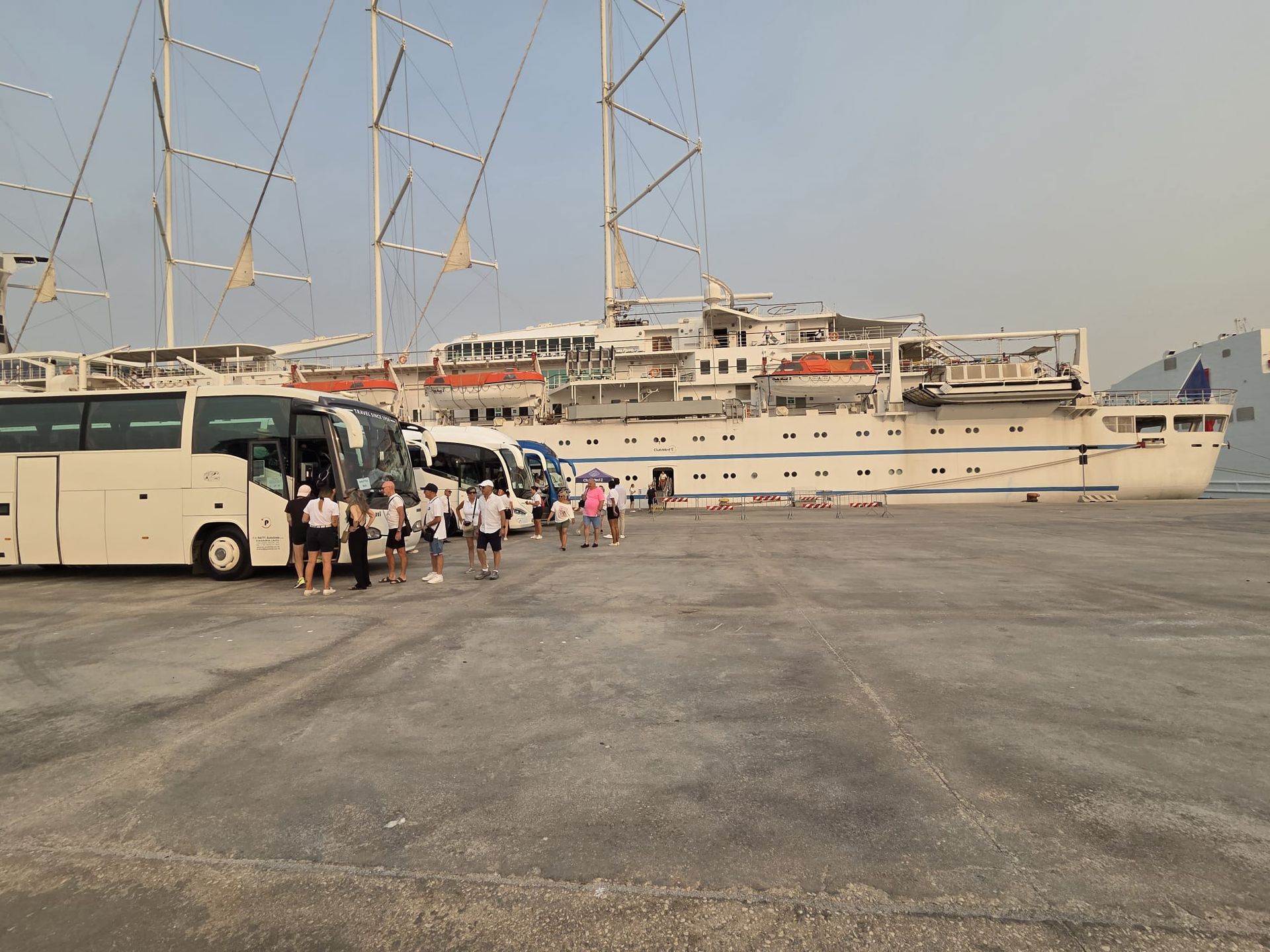 Persone che salgono su un autobus turistico bianco vicino a yacht ormeggiati in un porto.
