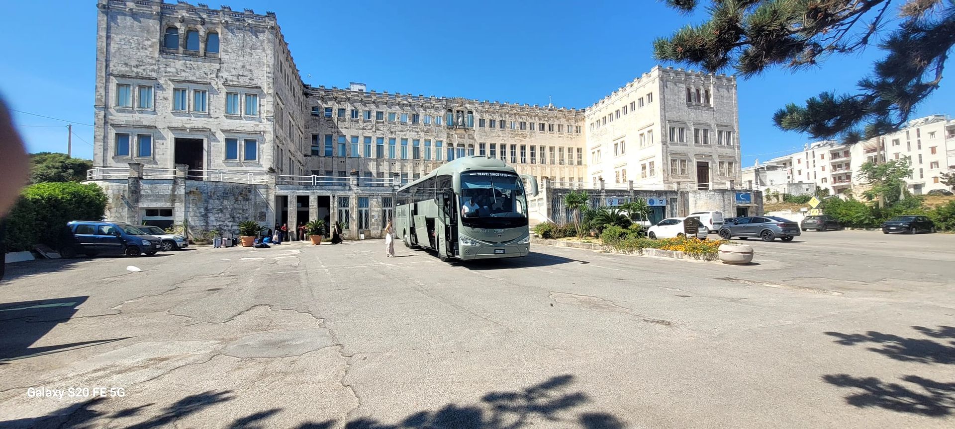 Ampia piazza con edifici storici e un autobus parcheggiato sotto un cielo azzurro e terso