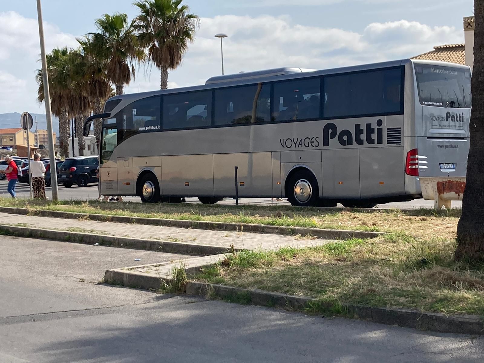 Pullman argentato e grigio parcheggiato lungo la strada, con palme e persone sullo sfondo