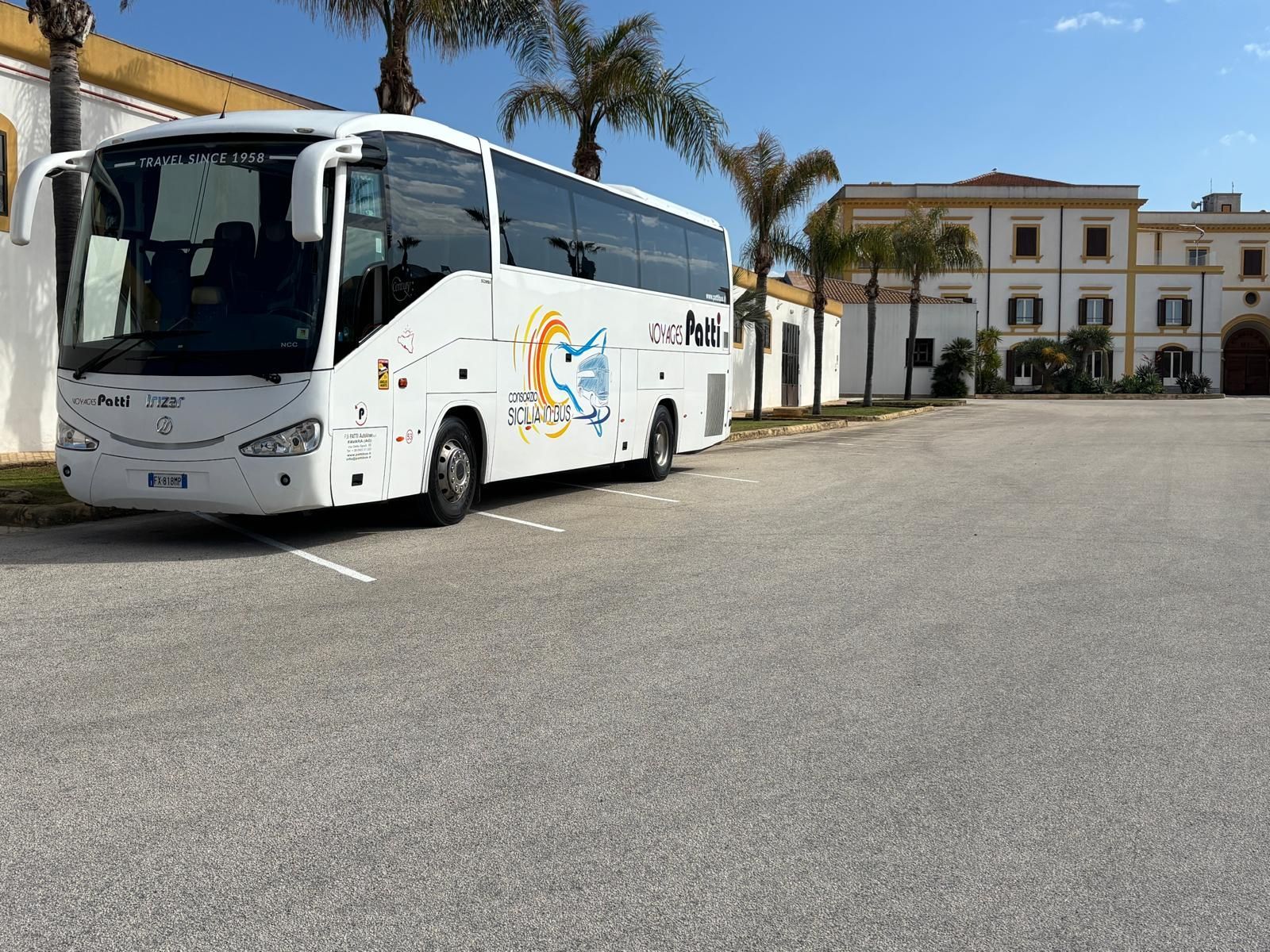 Autobus bianco da turismo parcheggiato davanti a un edificio fiancheggiato da palme, sotto un cielo sereno