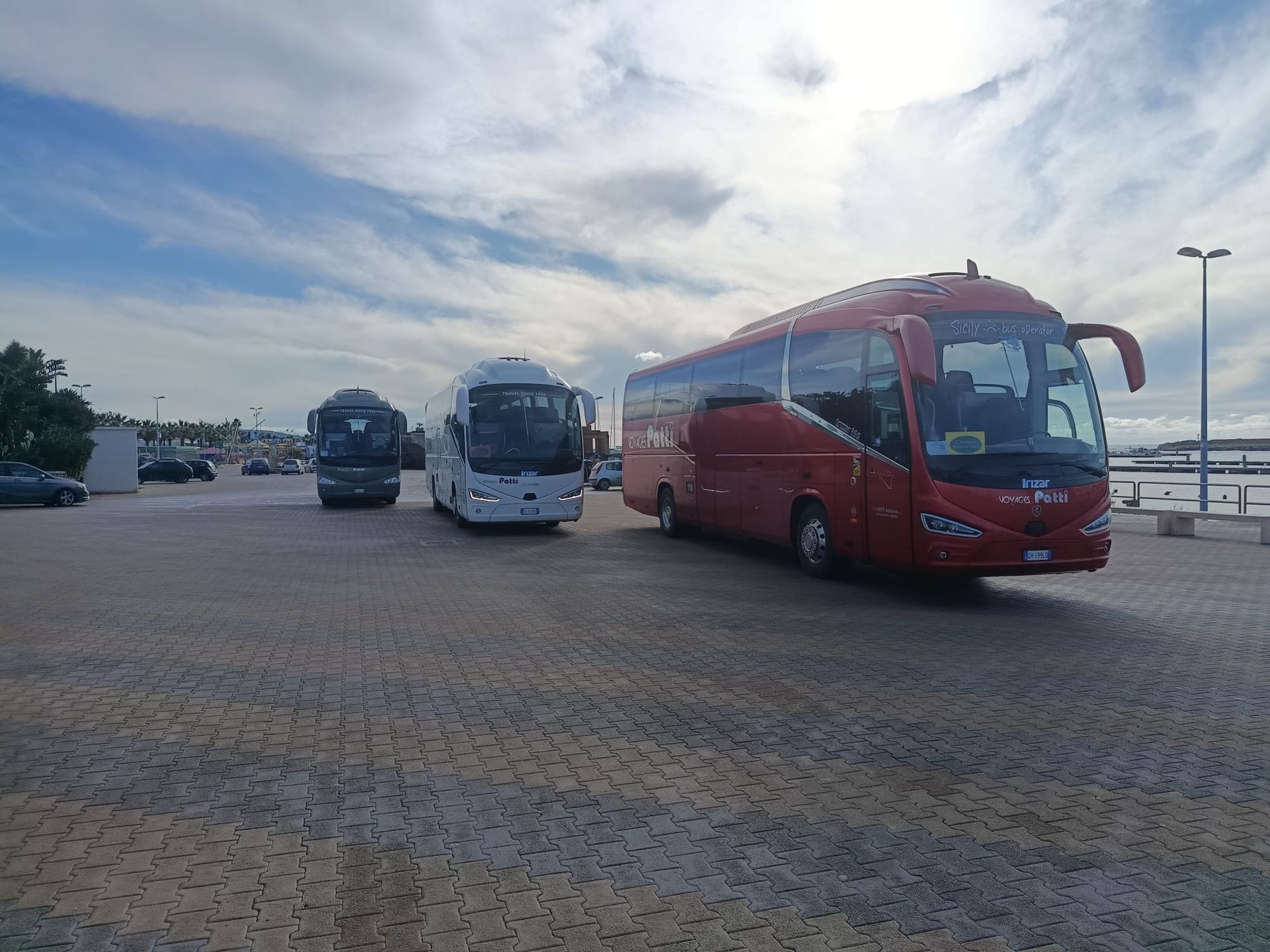 Pullman rosso parcheggiato in un piazzale asfaltato, con un altro pullman e il cielo nuvoloso sullo sfondo
