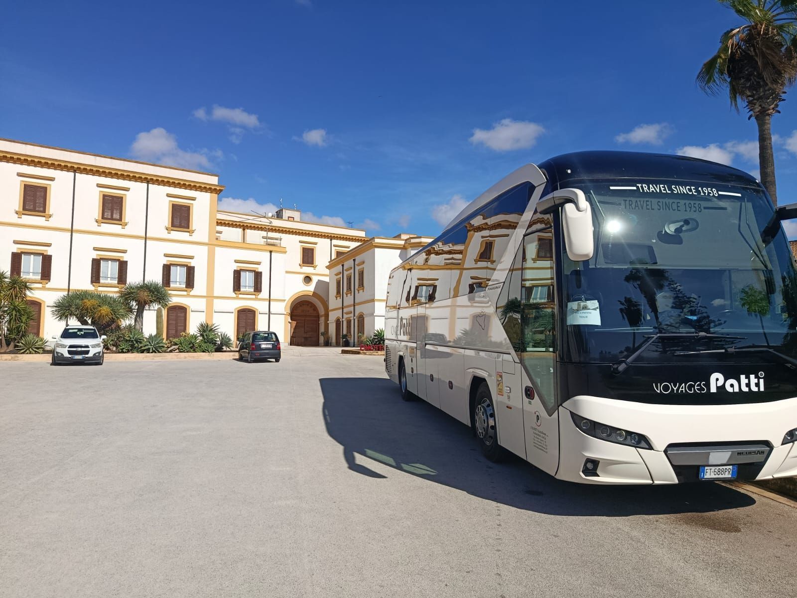 Pullman bianco parcheggiato davanti a un edificio storico illuminato dal sole, sotto un cielo azzurro