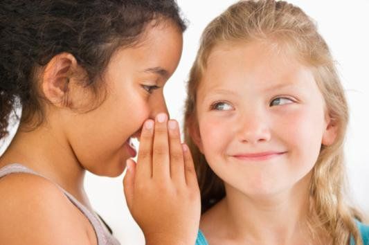 Two children whispering closely, one smiling in response