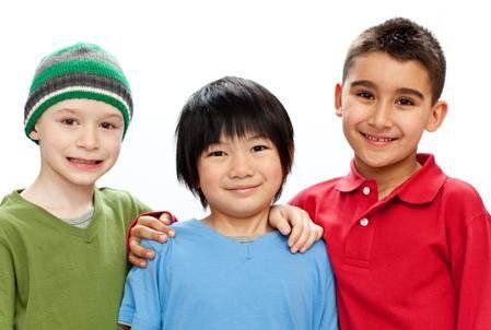 Three smiling children standing together, wearing green, blue, and red shirts, against a white background