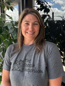 Smiling woman in a gray T-shirt standing indoors with plants in the background