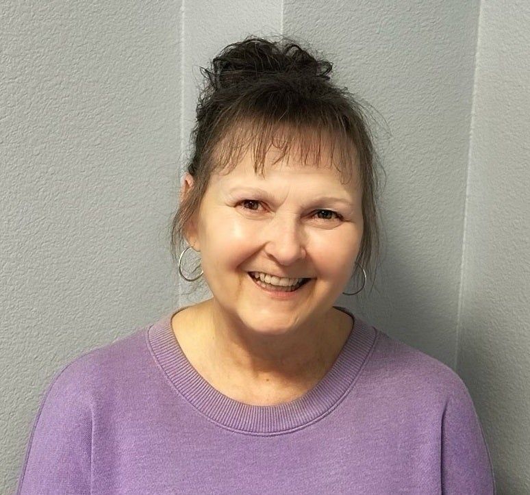 Smiling person in a purple sweater against a gray wall