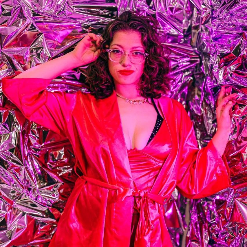 A woman in a red robe and glasses is standing in front of a foil wall.