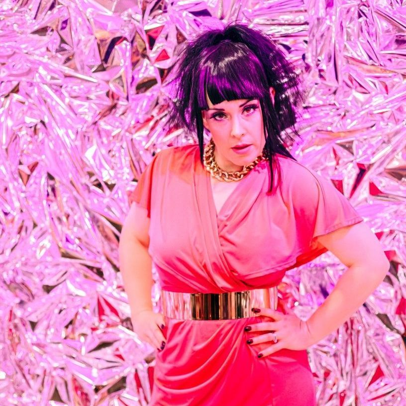 A woman in a pink dress is standing in front of a pink background.