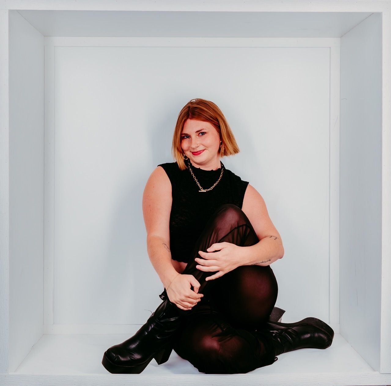 Woman in black outfit sits in white square.