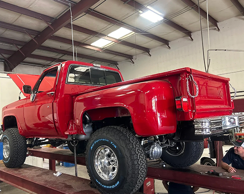Red pickup truck on a lift inside a garage, viewed from the rear side. | The Muffler Shop