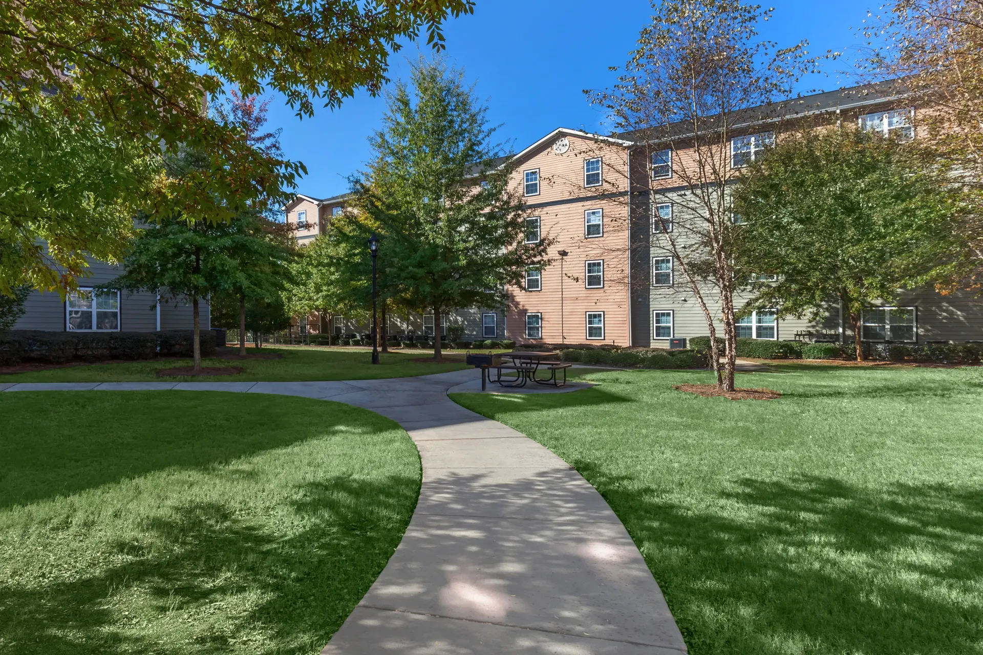 Walking path through manicured green lawn to apartment buildings with outdoor picnic area.