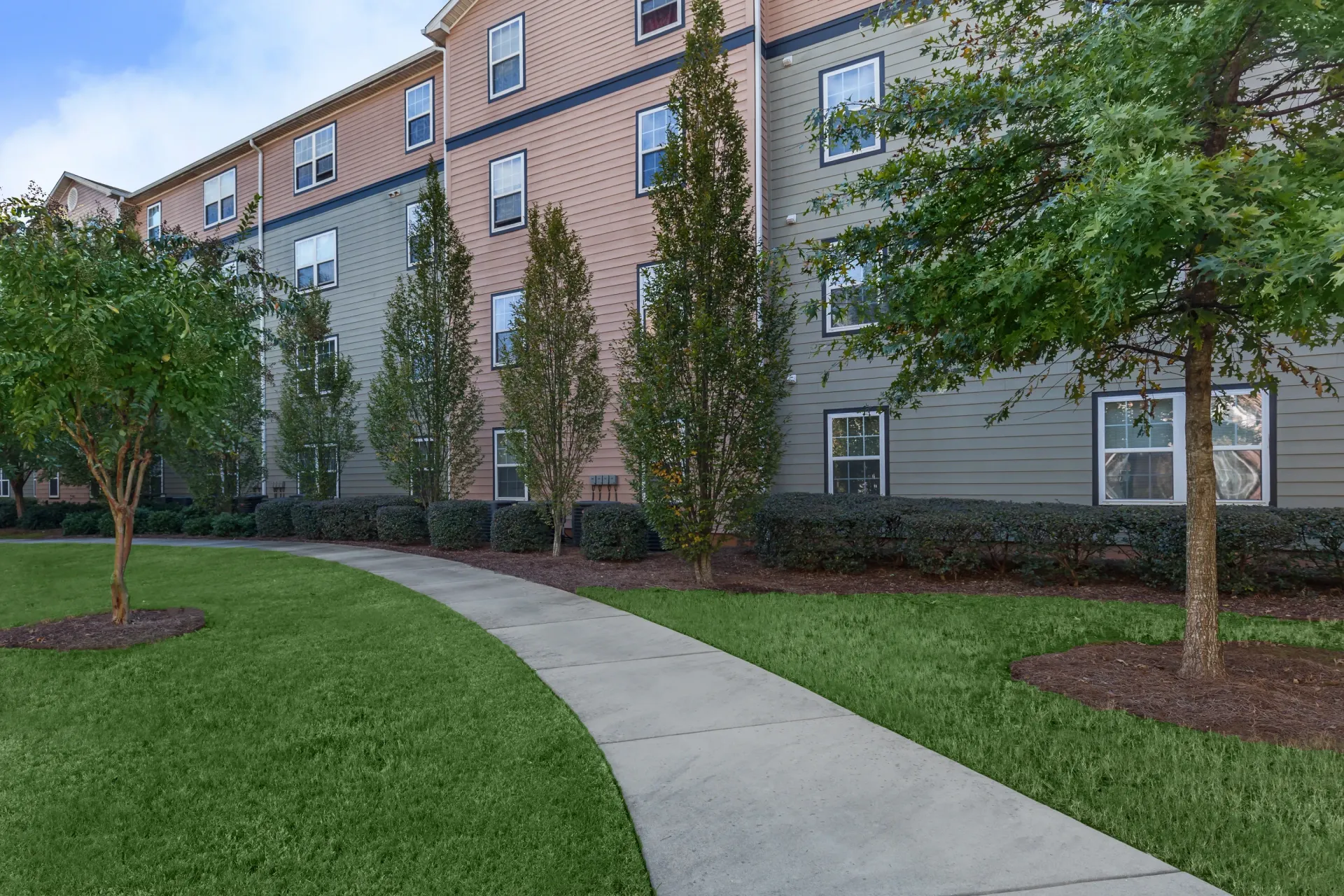 Apartment building exterior with a walking path and trees.