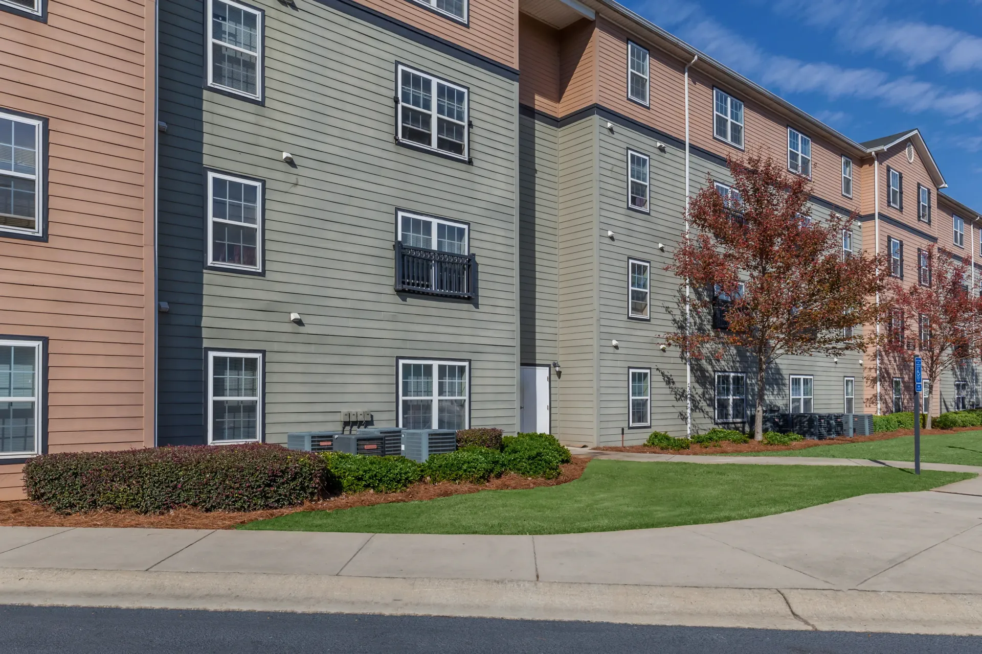 Exterior view of apartment buildings with tan and green siding, multiple windows, and a balcony.