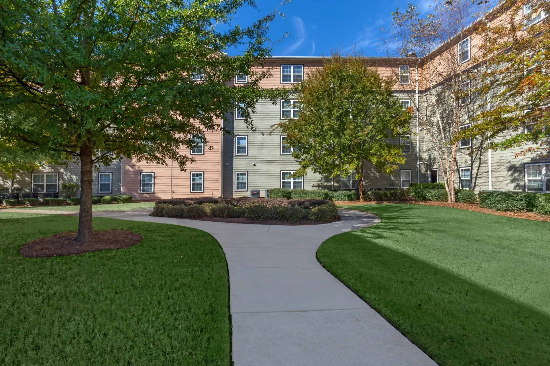 Exterior view of apartment buildings with a paved walkway and green lawn.