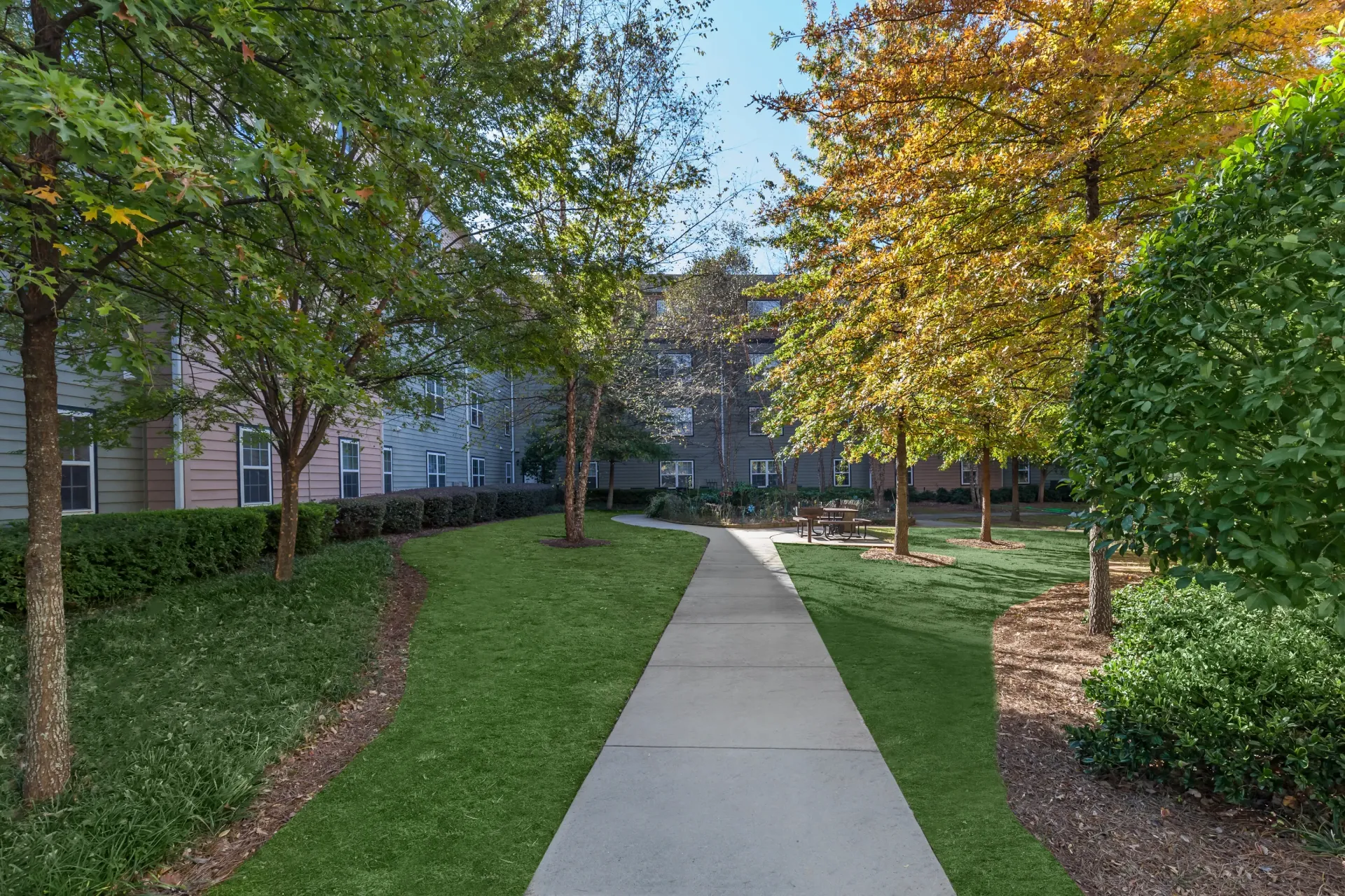 Pathway through a courtyard with trees and apartment buildings in the background.