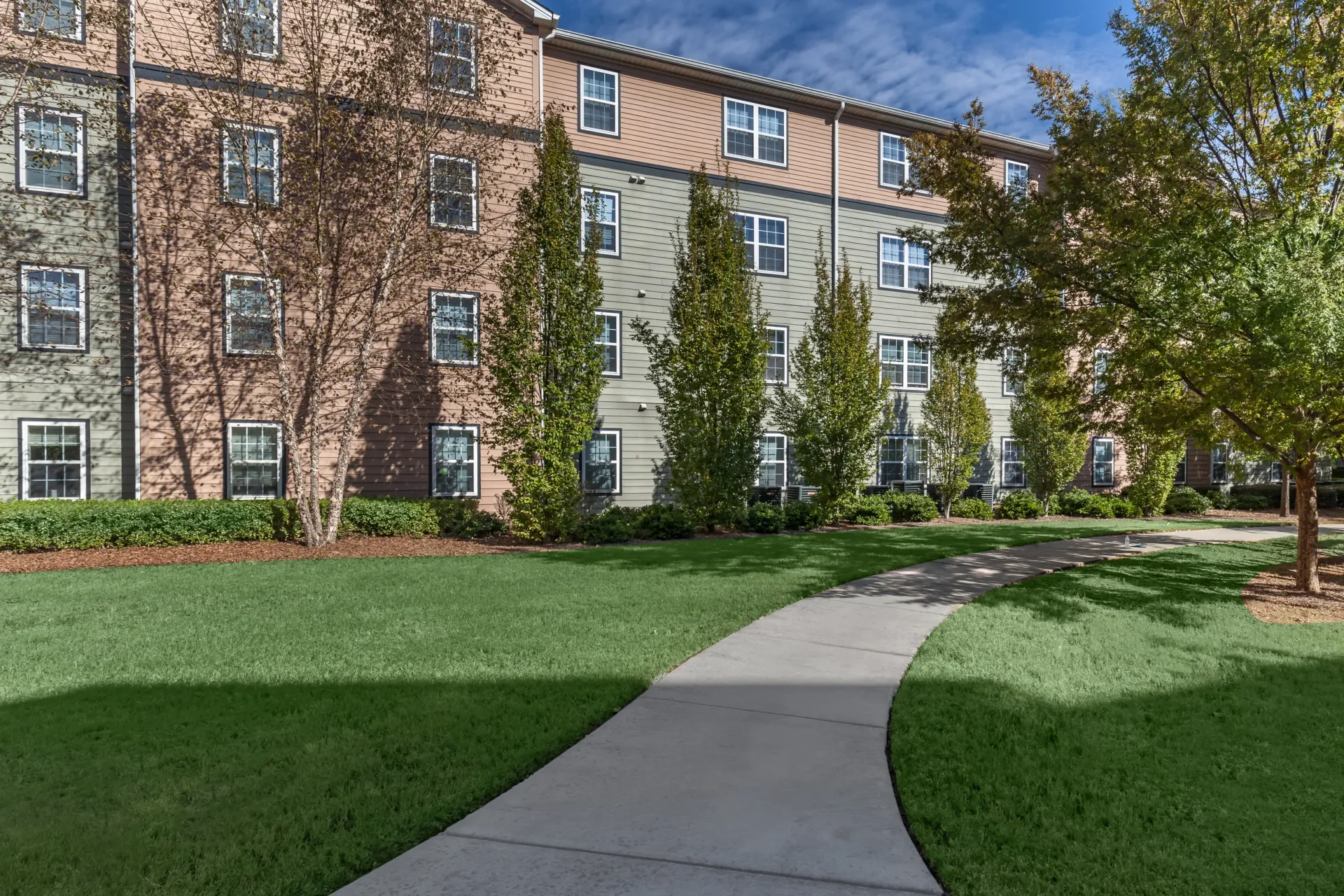 Exterior building view with a paved walkway through green grass and trees.
