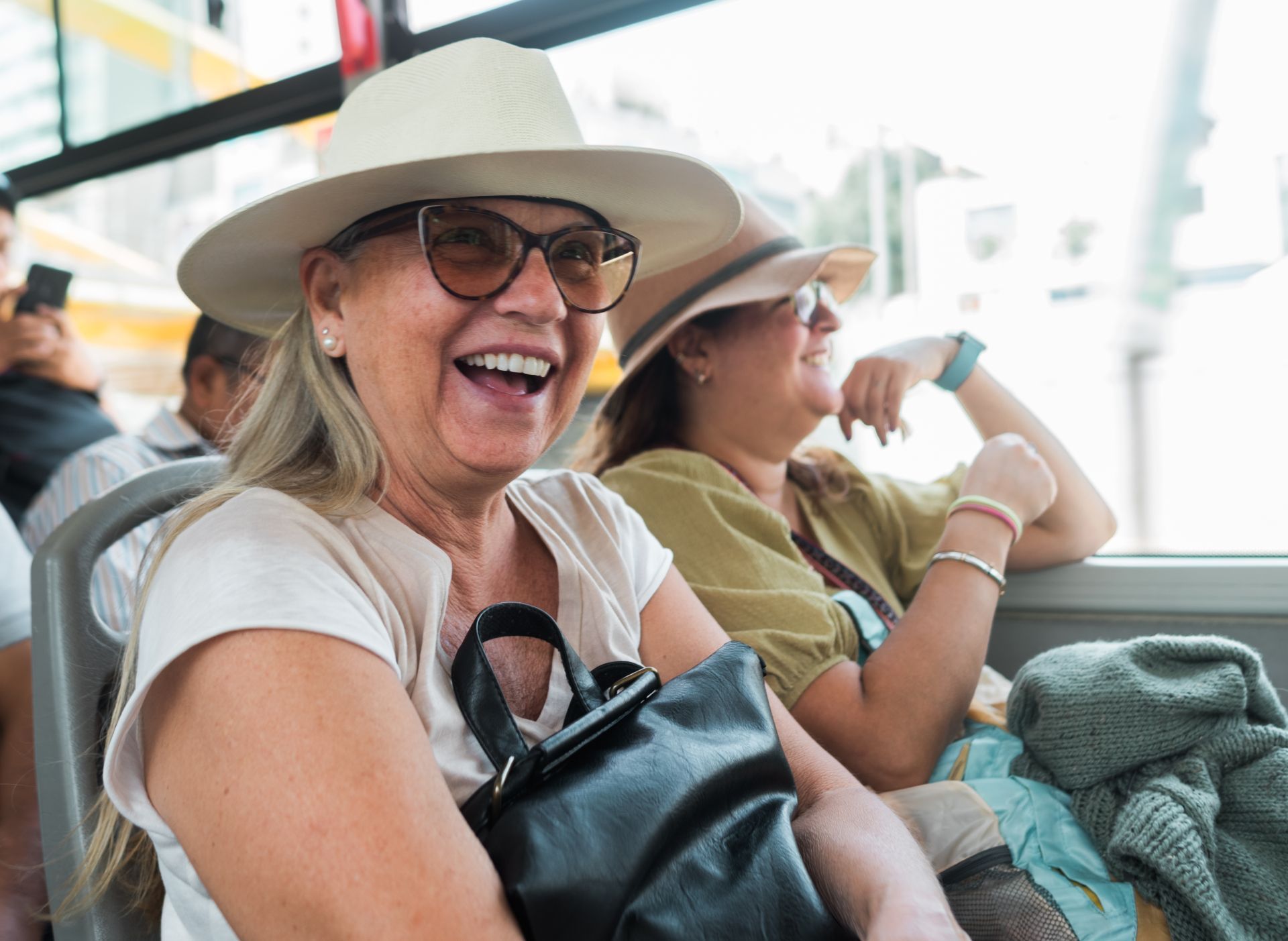 Smiling woman in a white hat and glasses sitting on a bench with bags in a bright waiting area