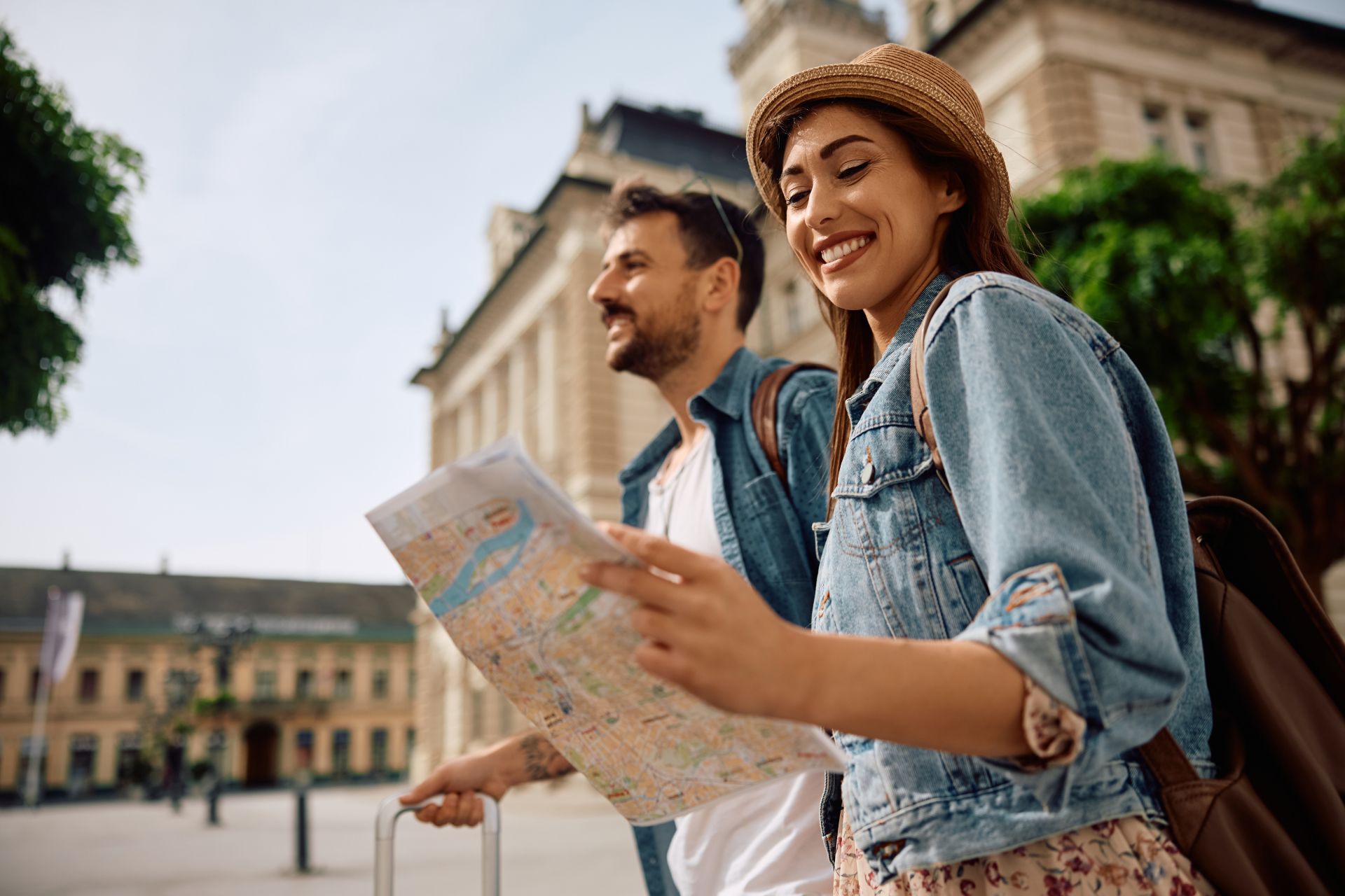 Two travelers smiling and studying a map in a city square with historic buildings behind them