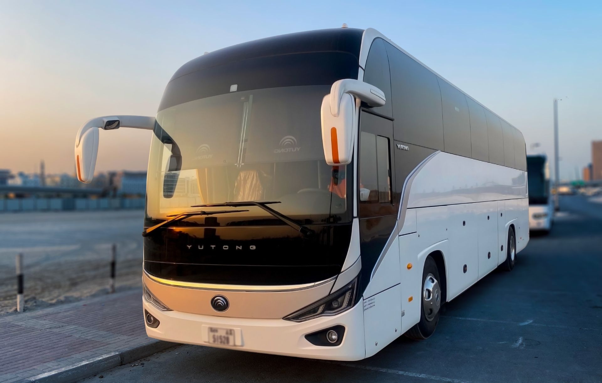 White coach bus parked on a road at sunset, front view with tinted windshield and side mirrors