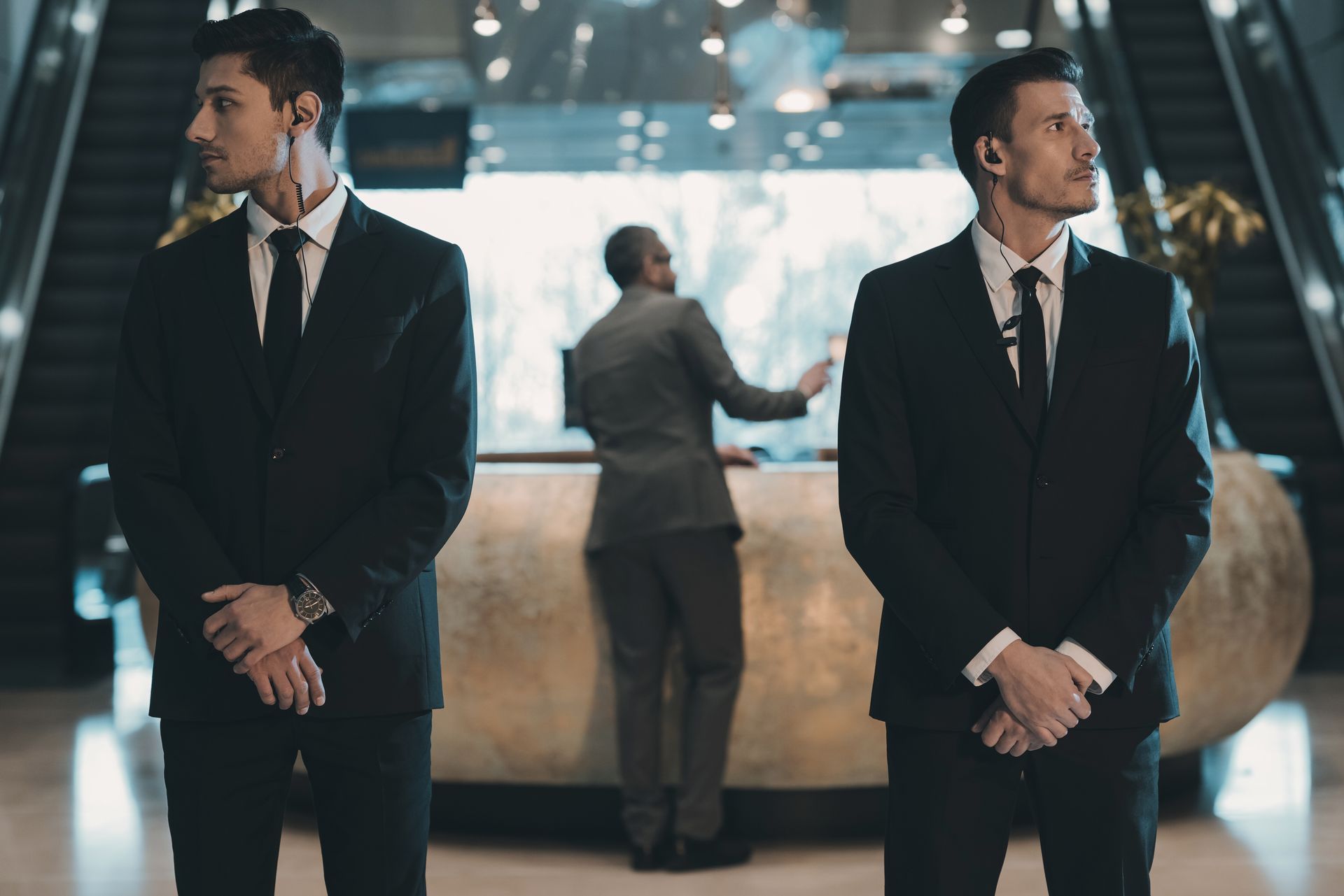 Two men in suits stand guard in a lobby; a receptionist stands behind a curved desk.