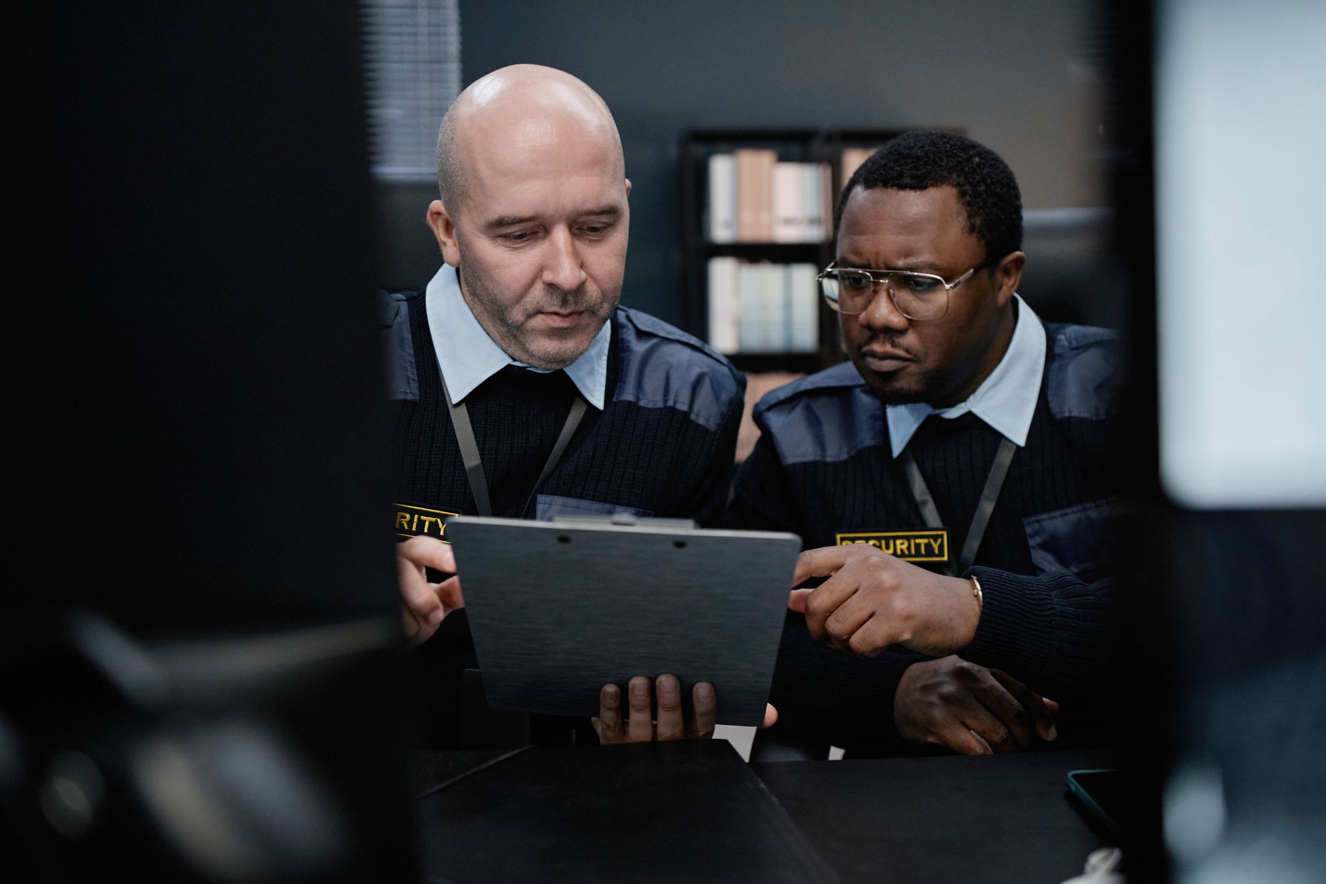 Two uniformed individuals examining a tablet, indoors. One points at the screen.