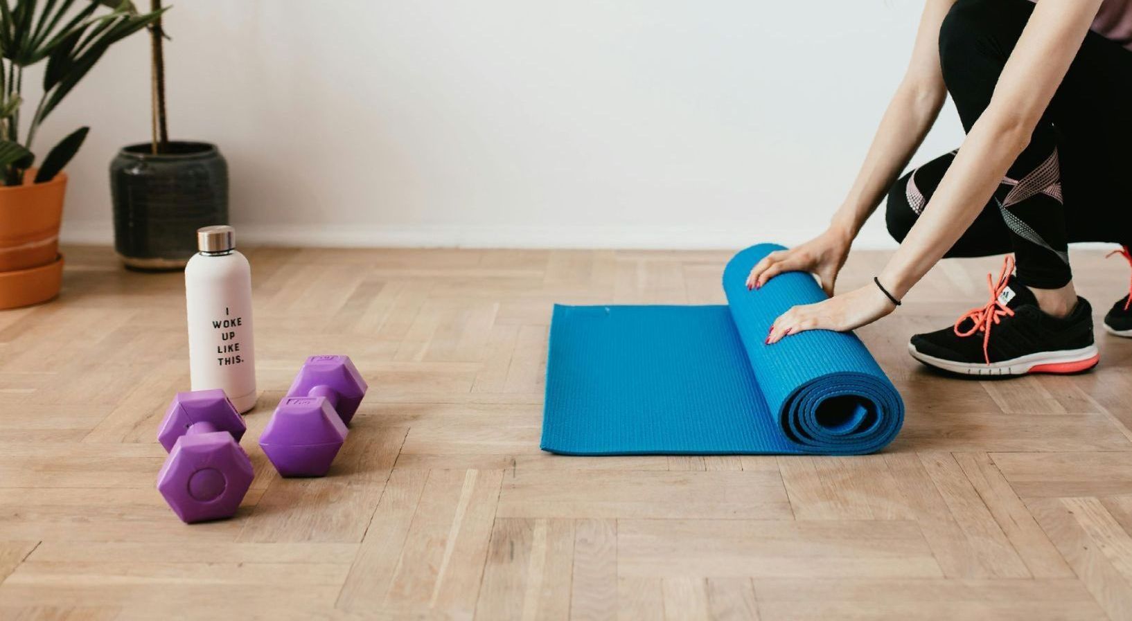 En kvinde knæler ned ved siden af ​​en yogamåtte og håndvægte.