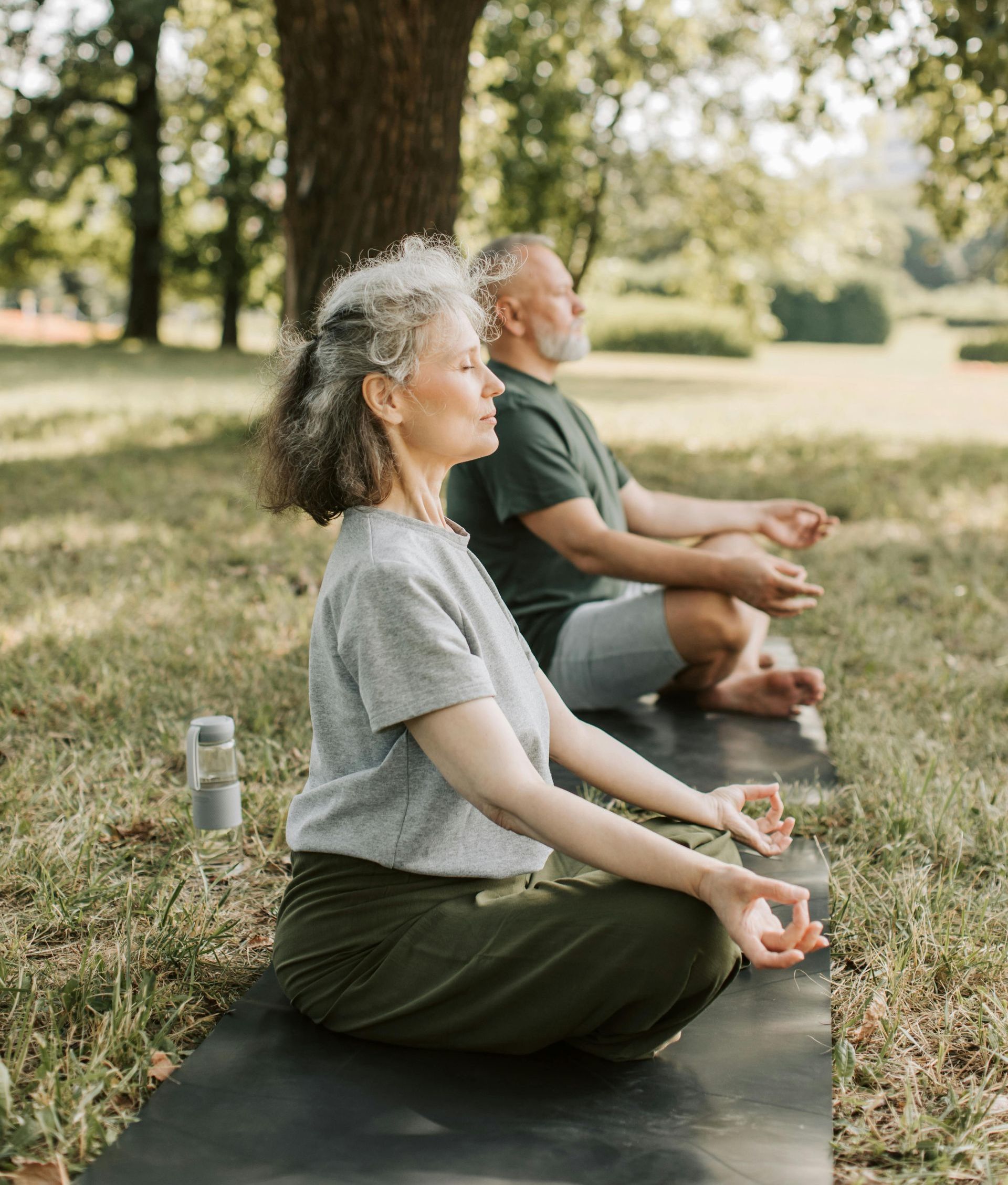 En mand og en kvinde sidder på en yogamåtte i en park.