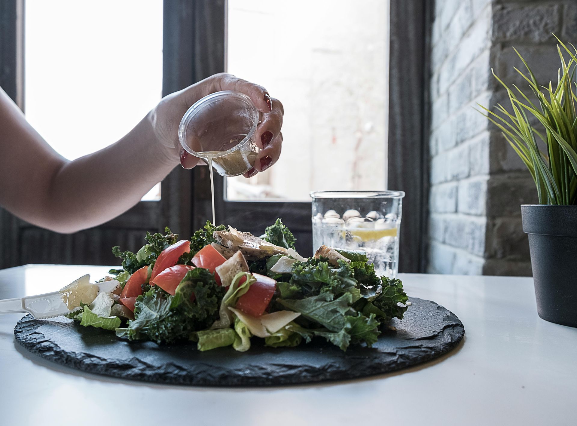 En person hælder dressing på en salat på et bord.