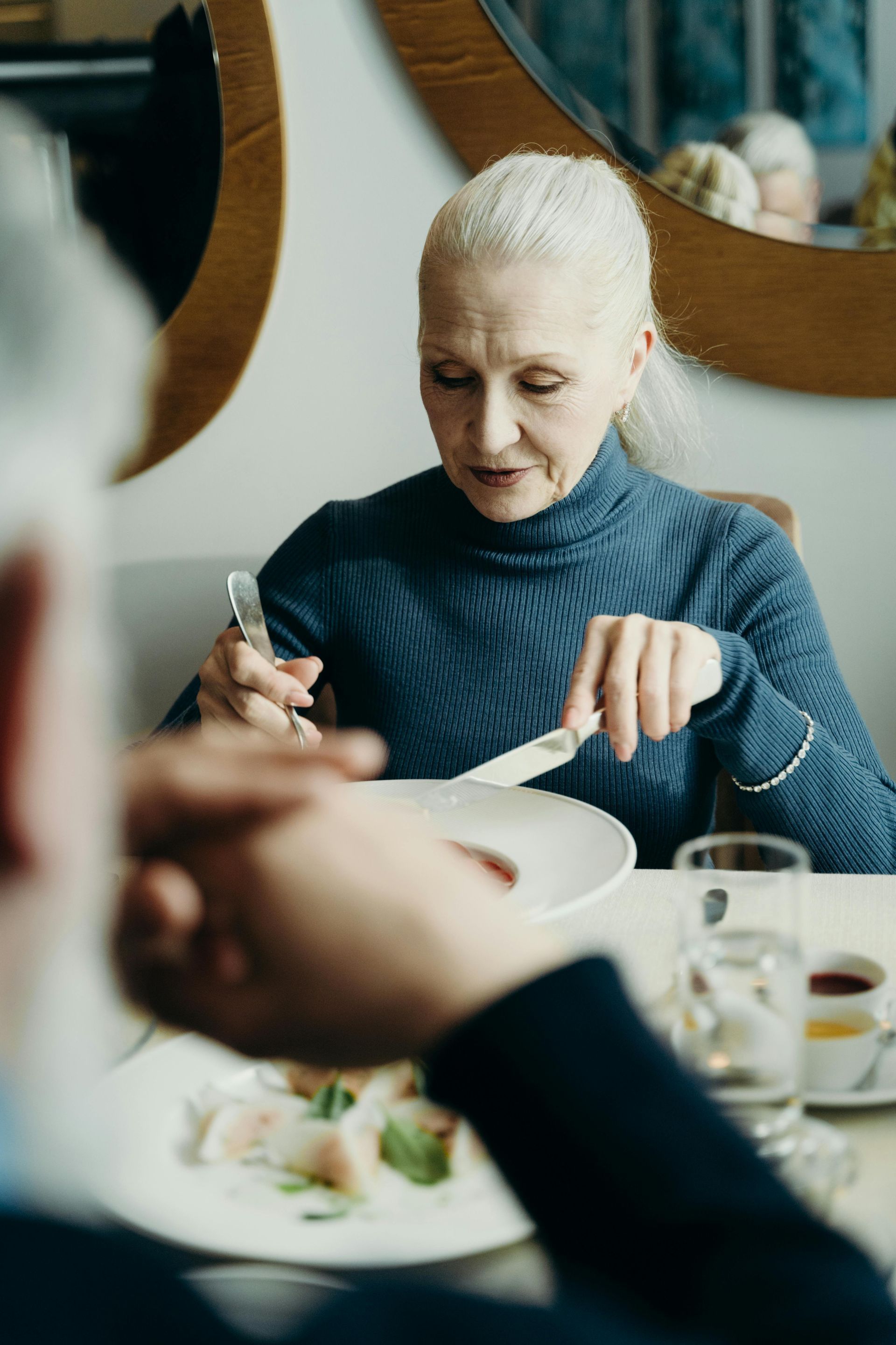 En ældre kvinde sidder ved et bord og spiser et måltid.