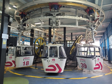 Une station circulaire montre des télécabines blanches numérotées 18, 39 et d'autres se déplaçant le long d'un système de rails aériens.