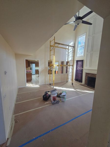 Room under renovation with scaffolding, tools, and fireplace. Sunlight streams through tall windows.