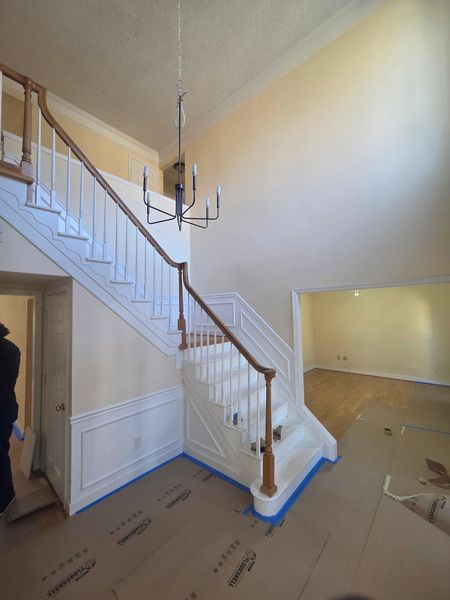 Interior view of a staircase and entryway with white risers, wooden handrails, and a chandelier; light yellow walls.