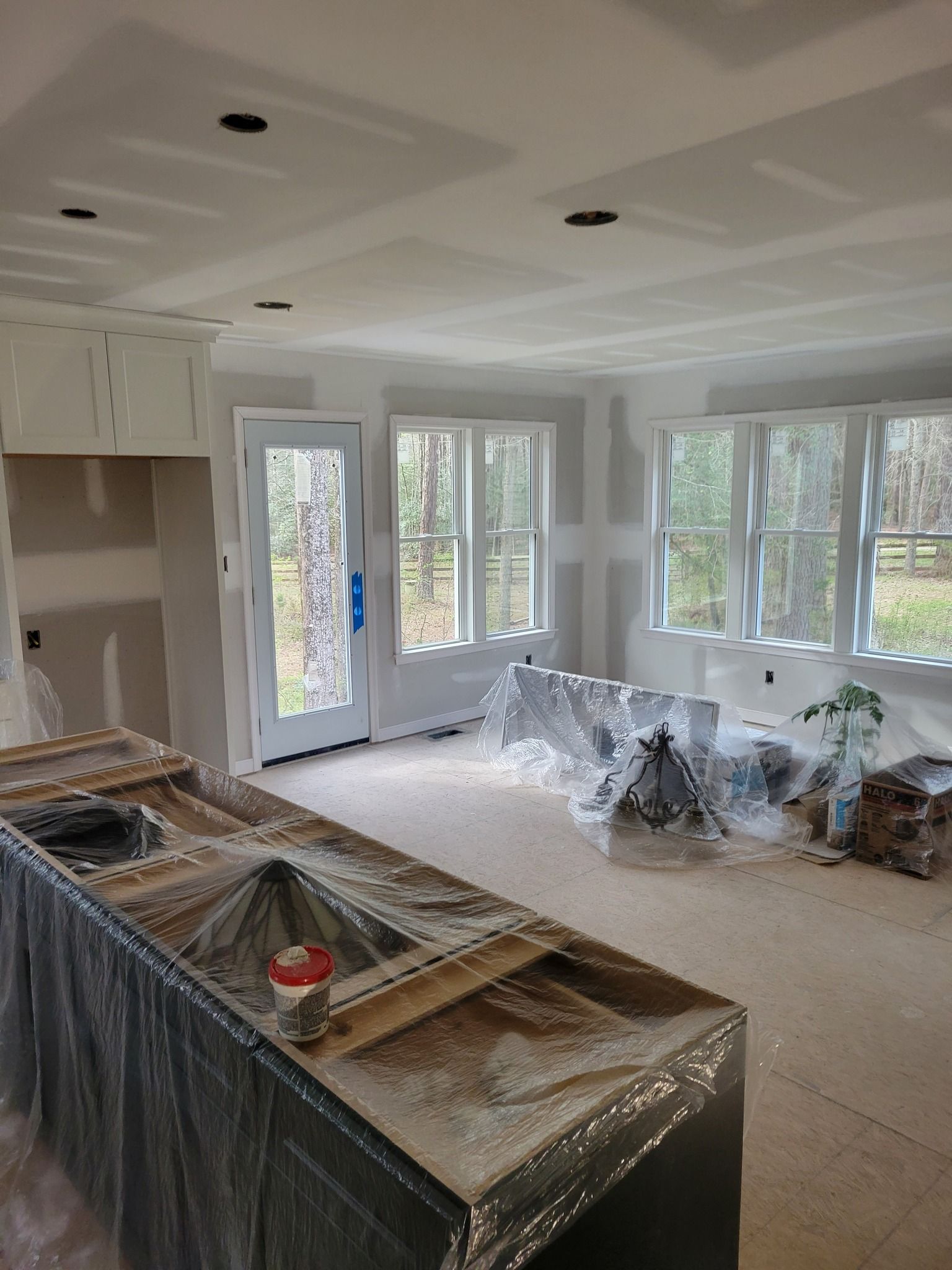 Interior of a kitchen under construction, with drywall, windows, and covered countertops.