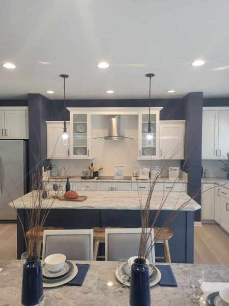 Modern kitchen with dark blue island, white cabinets, pendant lights, and a dining table in the foreground