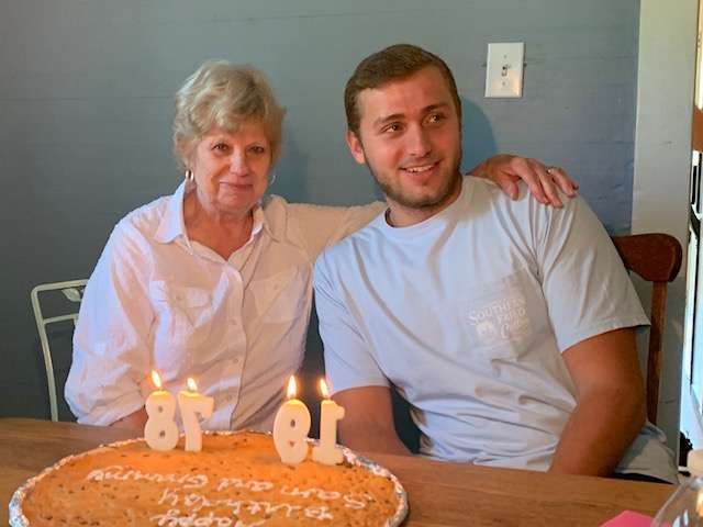 Two people seated at a table with a birthday cake and lit candles, smiling indoors