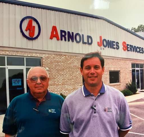 Two men standing outside Arnold Jones Services building under the company sign.