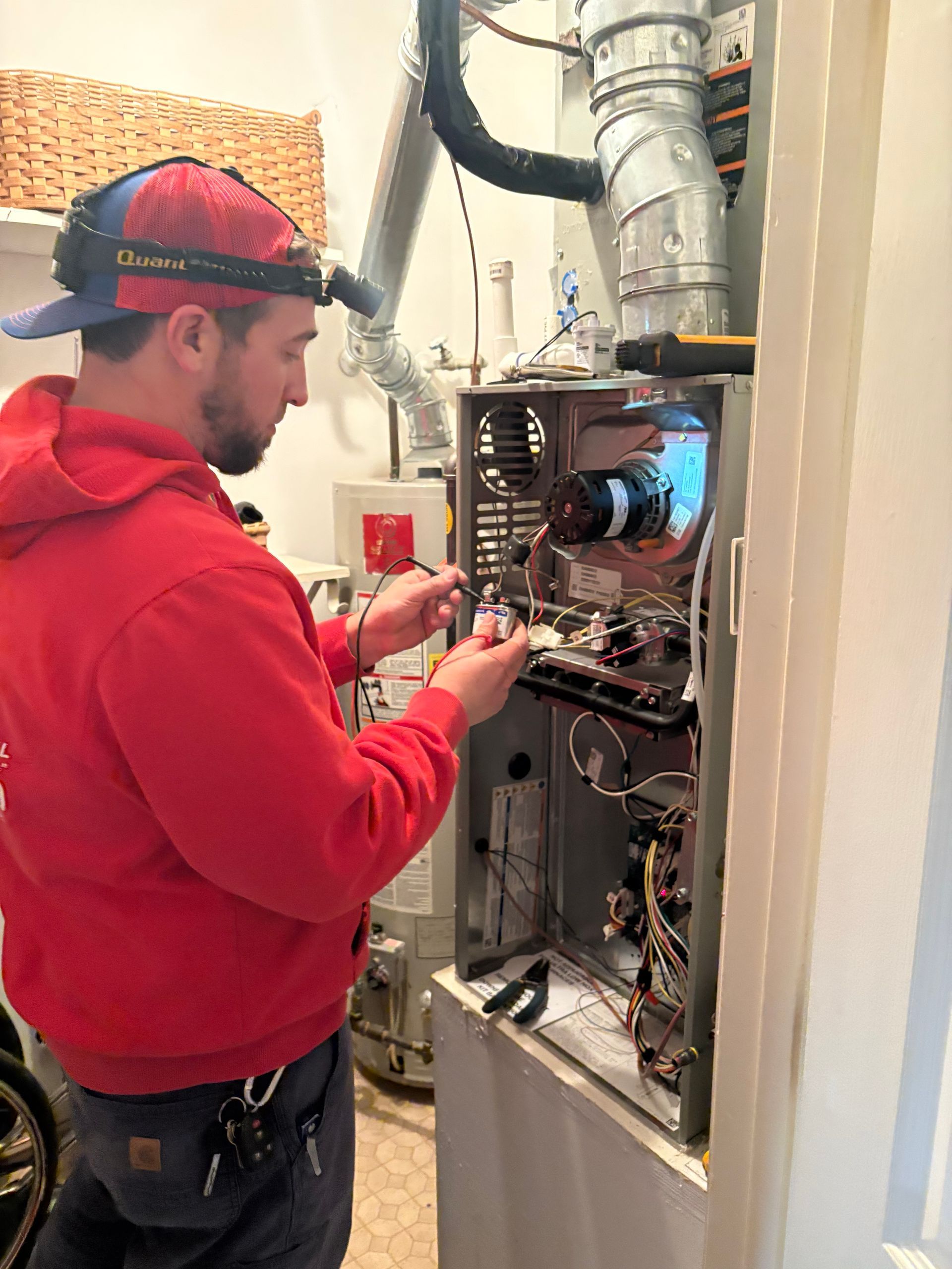 Technician in red hoodie inspecting open electrical panel with wires and components inside utility room