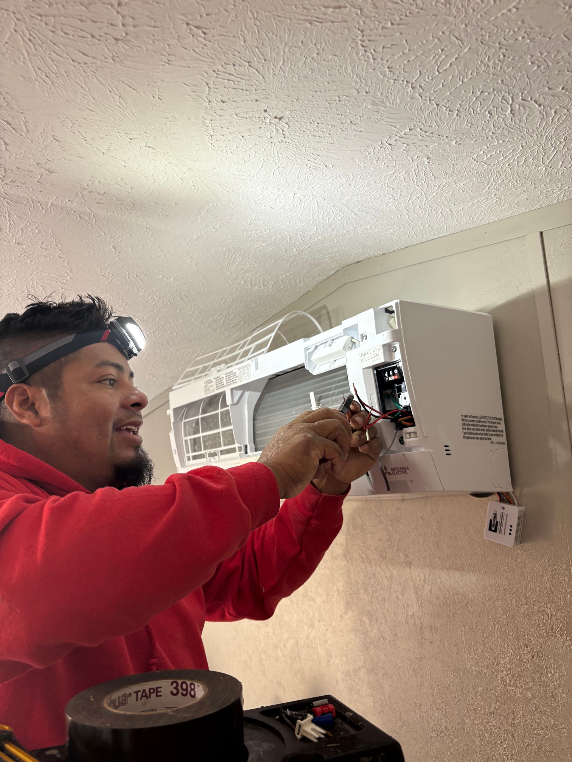 Technician in red shirt repairing a wall-mounted air conditioner indoors.