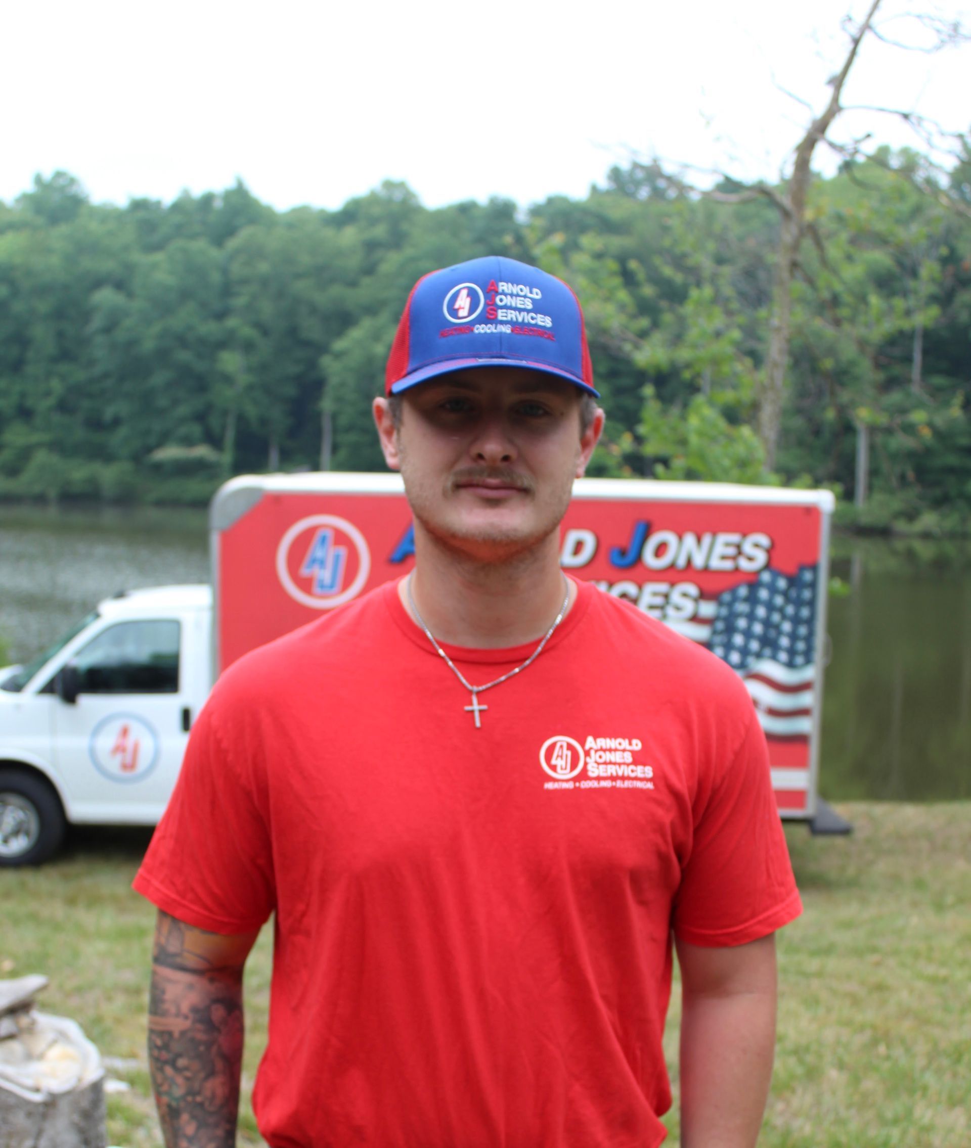 Man in red shirt and blue cap standing outdoors in front of a truck and sign