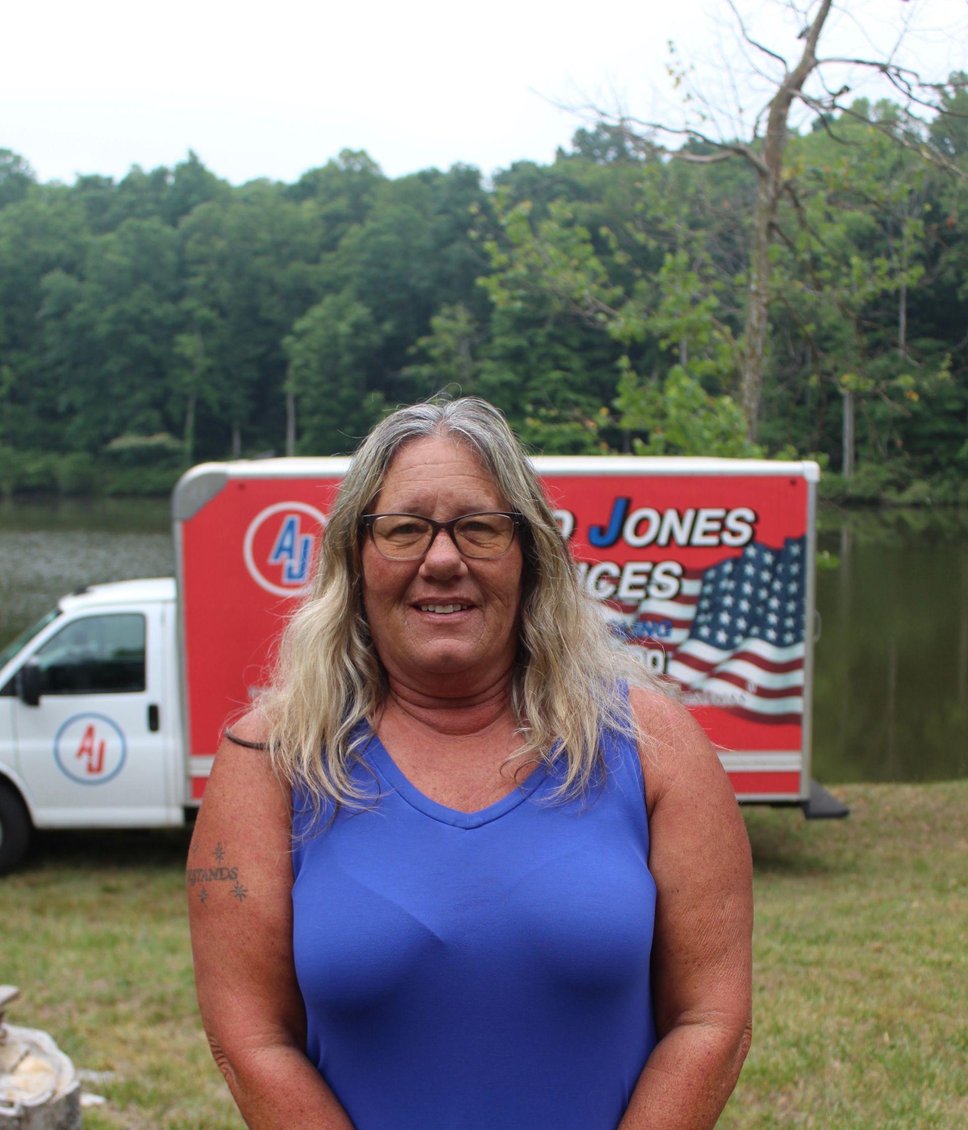 Woman in blue shirt smiling outdoors in front of a Jones services truck by the water