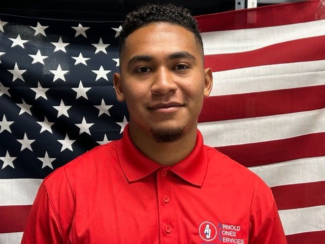 Man in a red polo shirt standing before an American flag backdrop