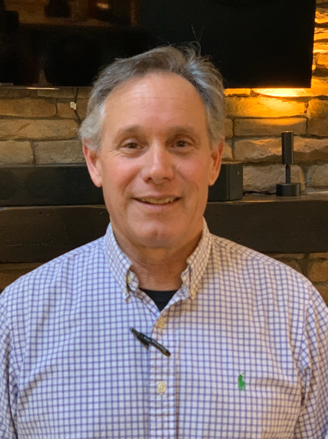 Man in a gray polo shirt smiling outdoors in front of a brick building