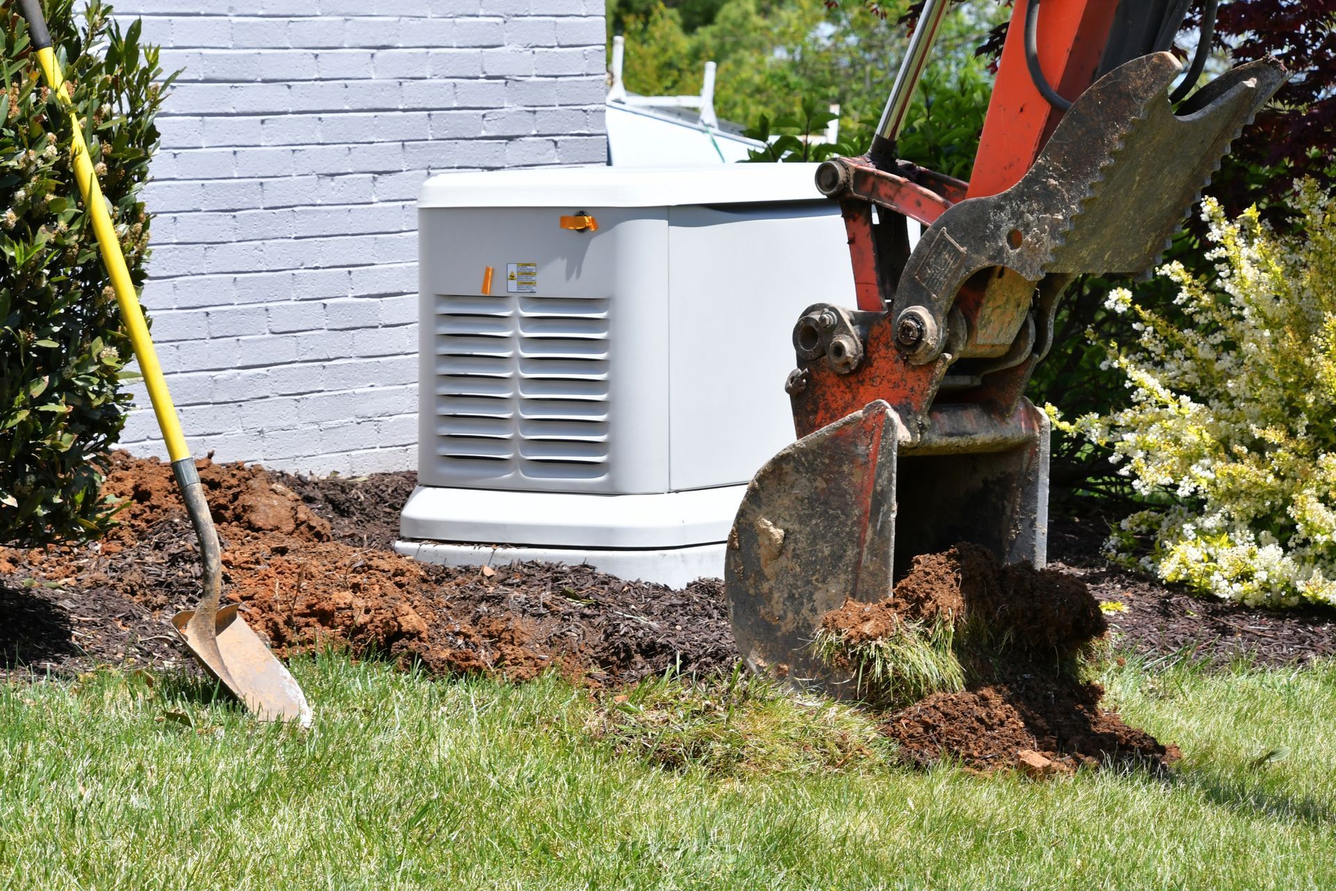 Excavator digging soil beside a house with a shovel and patch of grass in the foreground