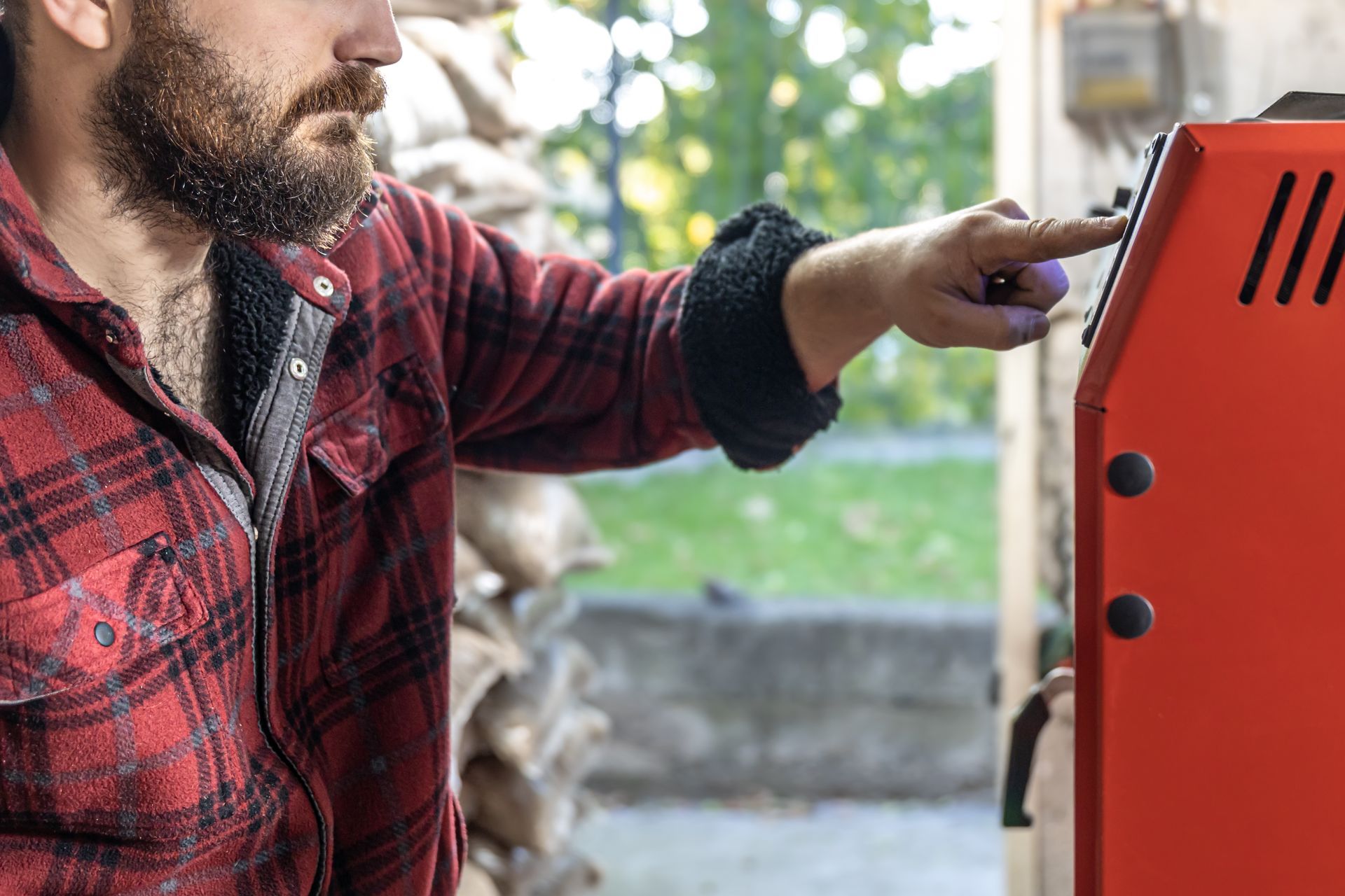 Man in red plaid jacket pointing at an orange machine outdoors