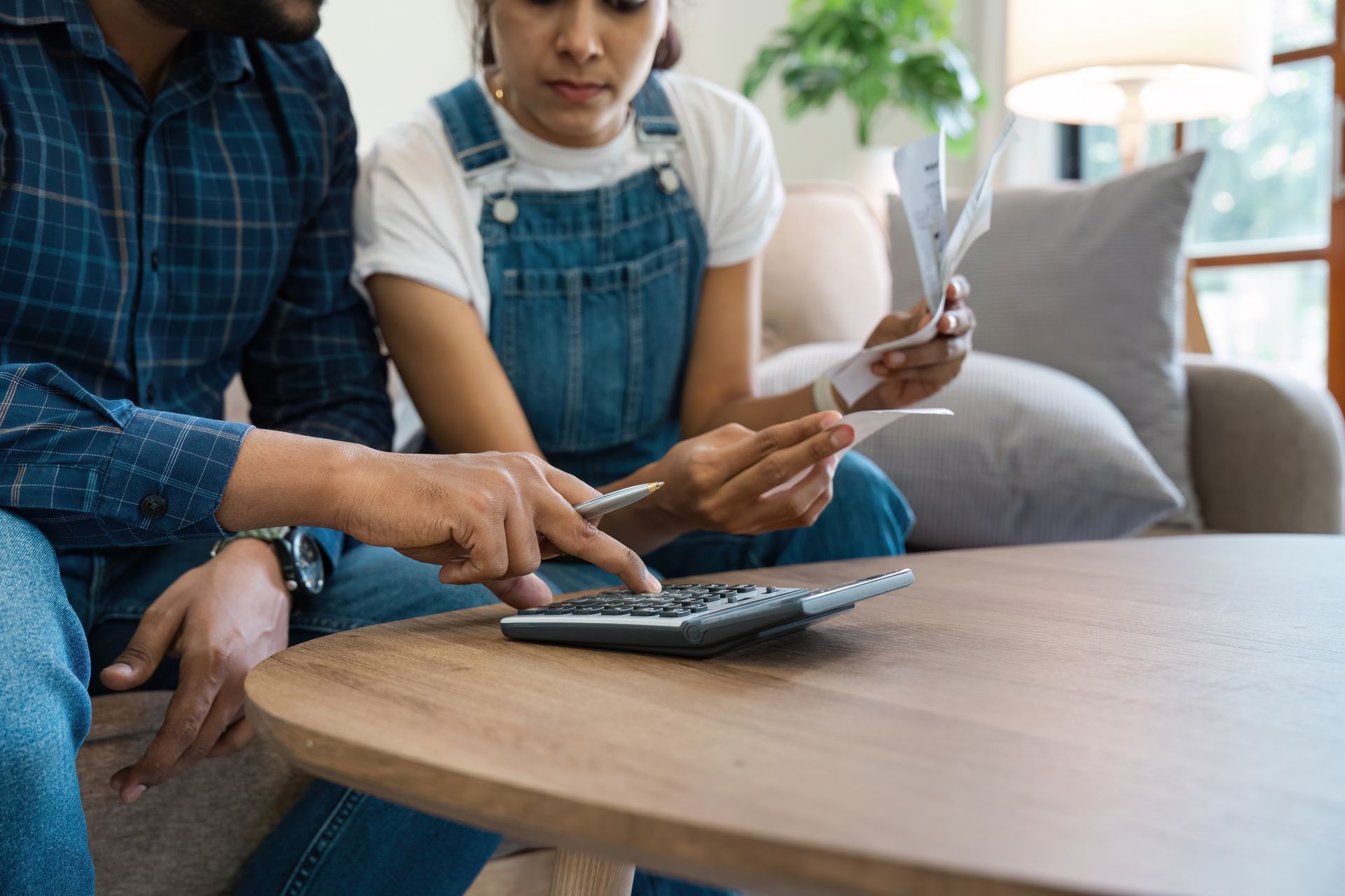 Two people using a remote and calculator at a table in a bright living room