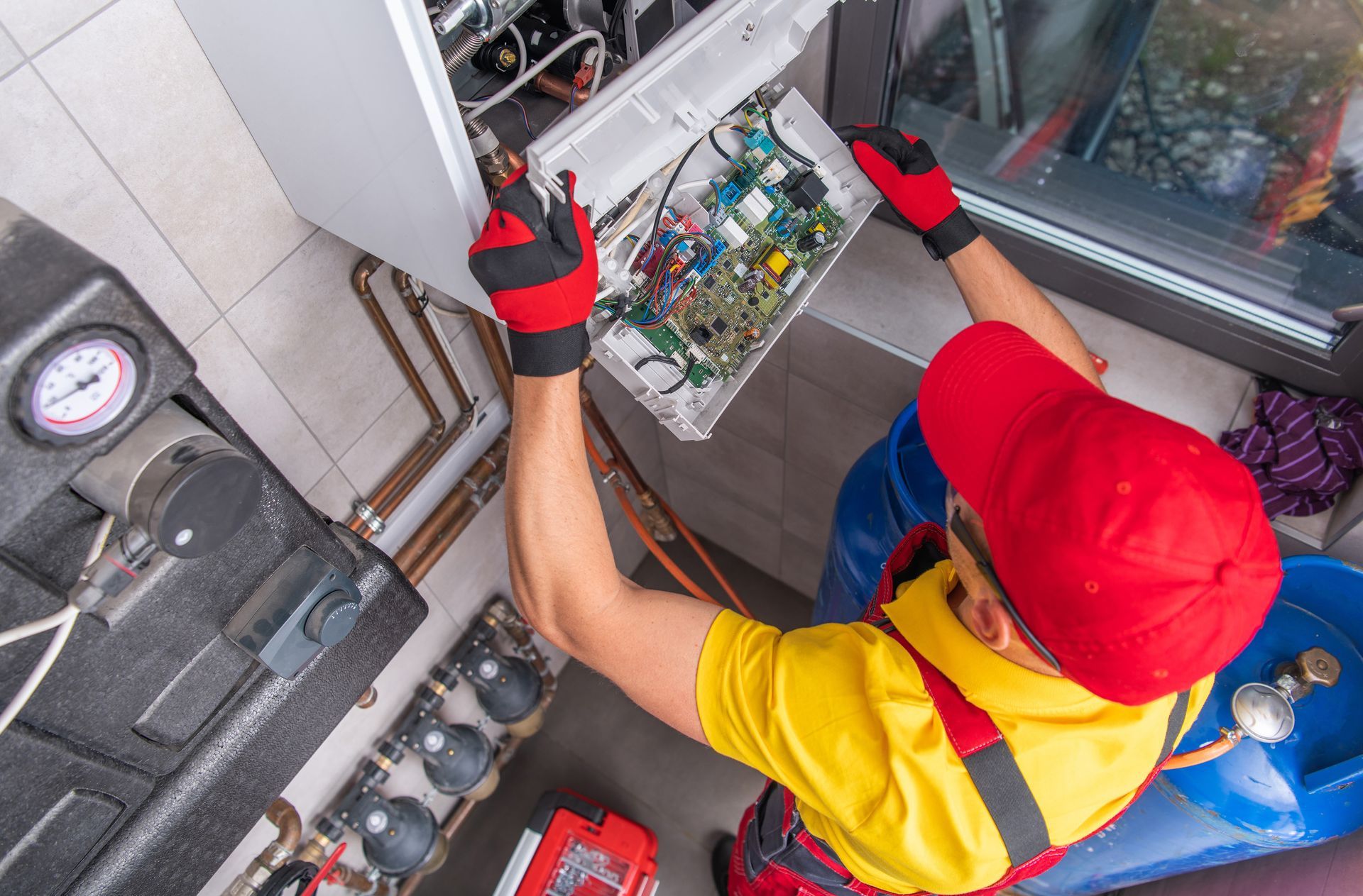 Technician in red cap and gloves repairing wiring inside an electrical control panel.