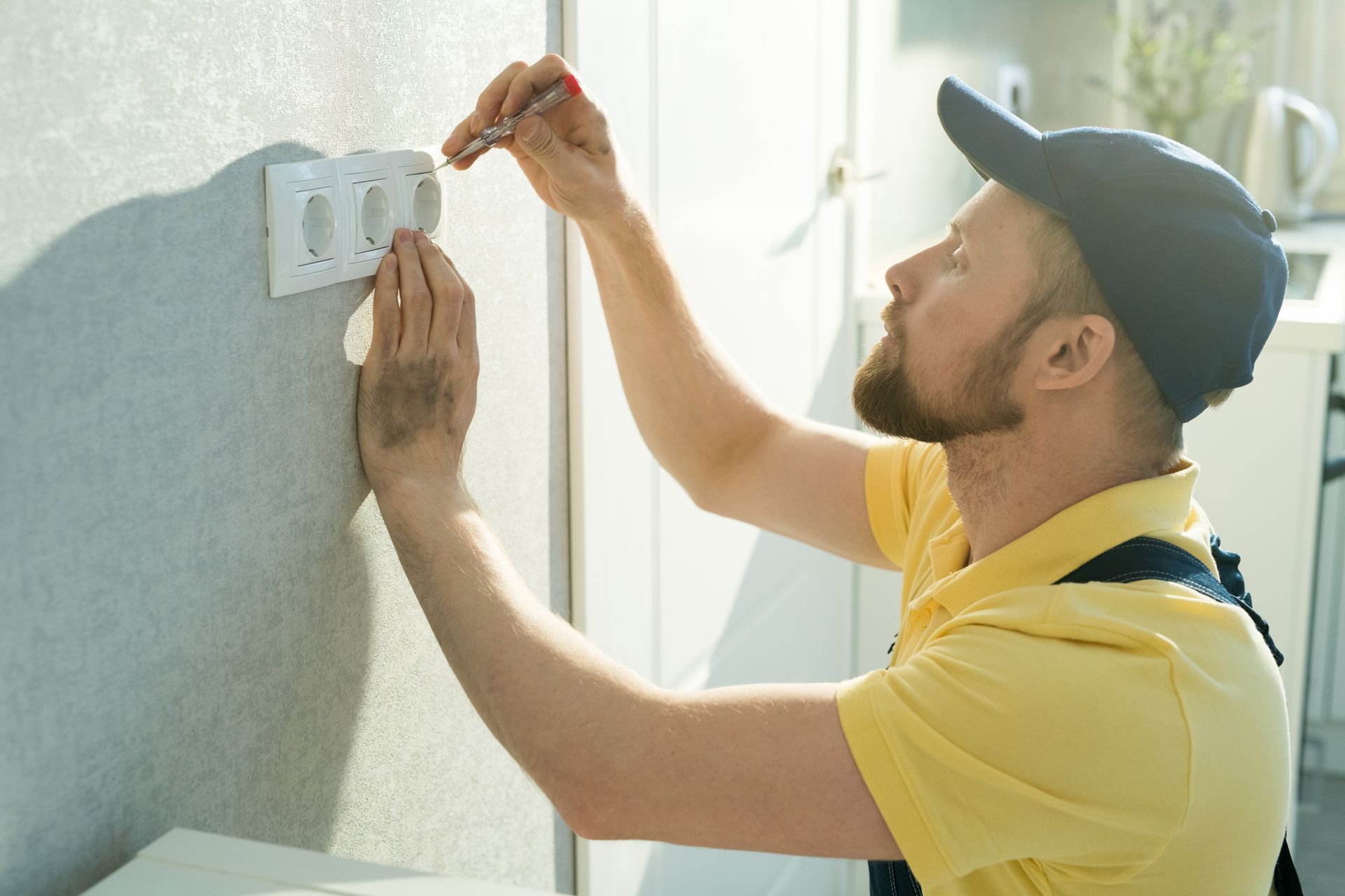 Worker in yellow shirt and black cap measuring a wall with a tape measure