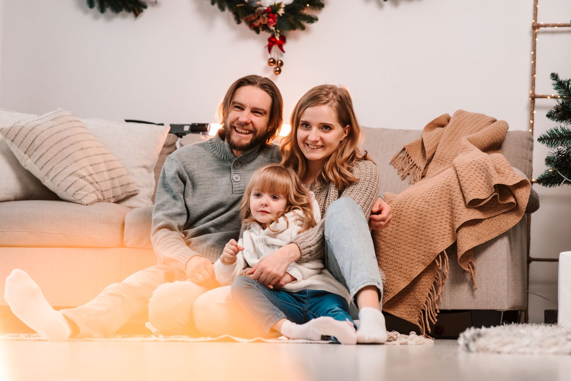 Family sitting on a couch with a child, wrapped in a cozy blanket, in a softly lit living room