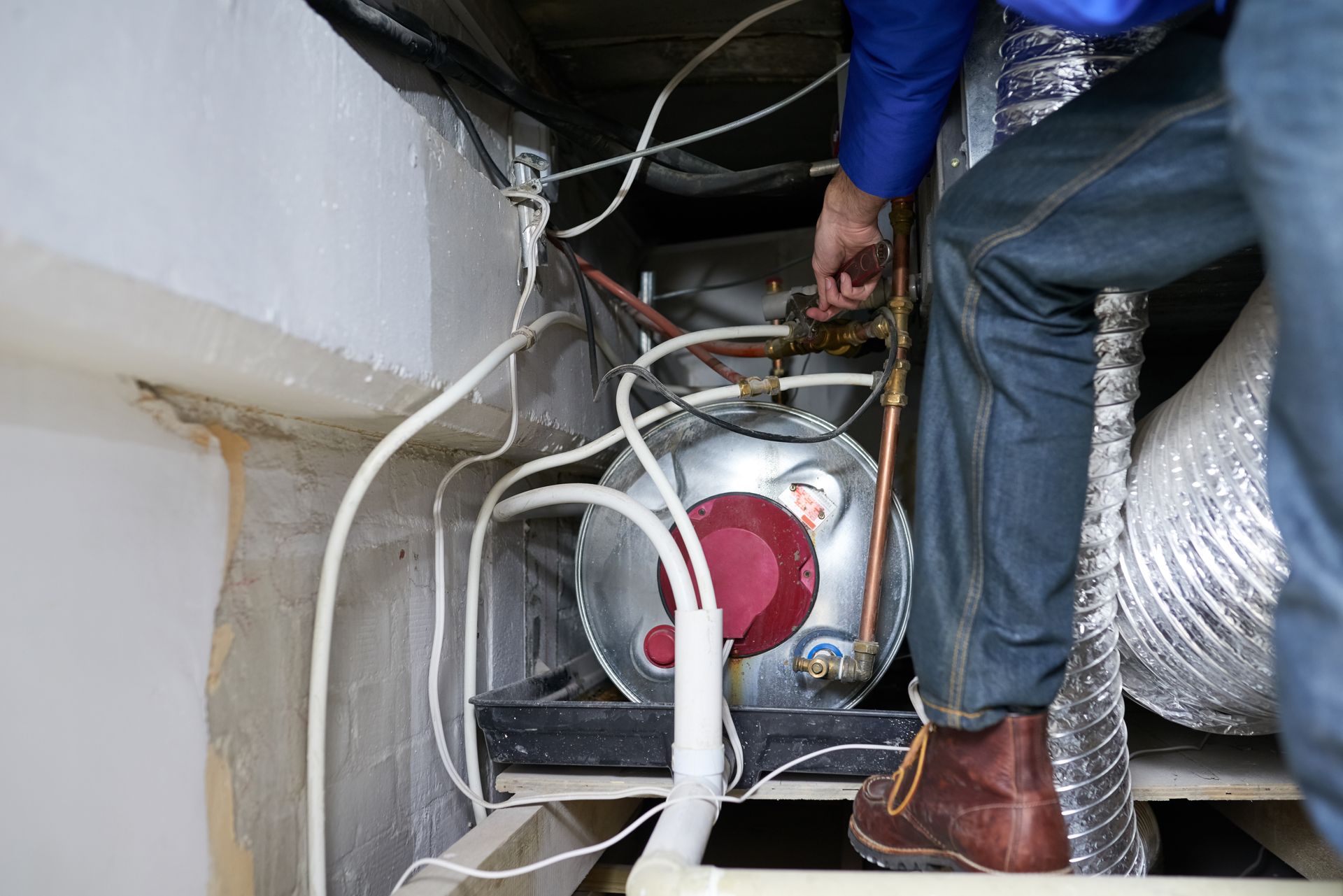 Technician working under a floor, handling wiring beside a fan and ductwork